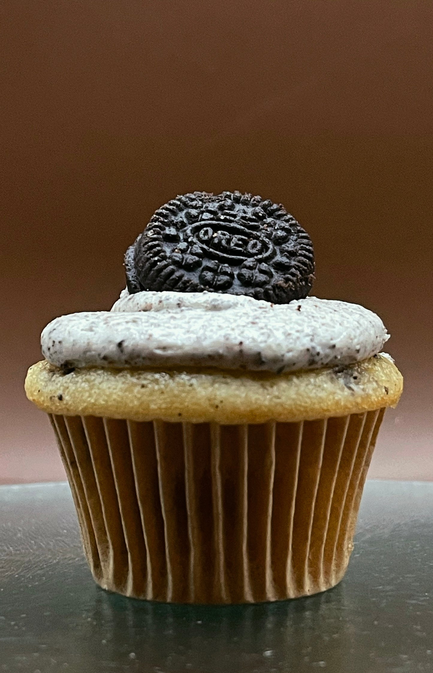 Cupcake with Oreo frosting and cookie on a brown background